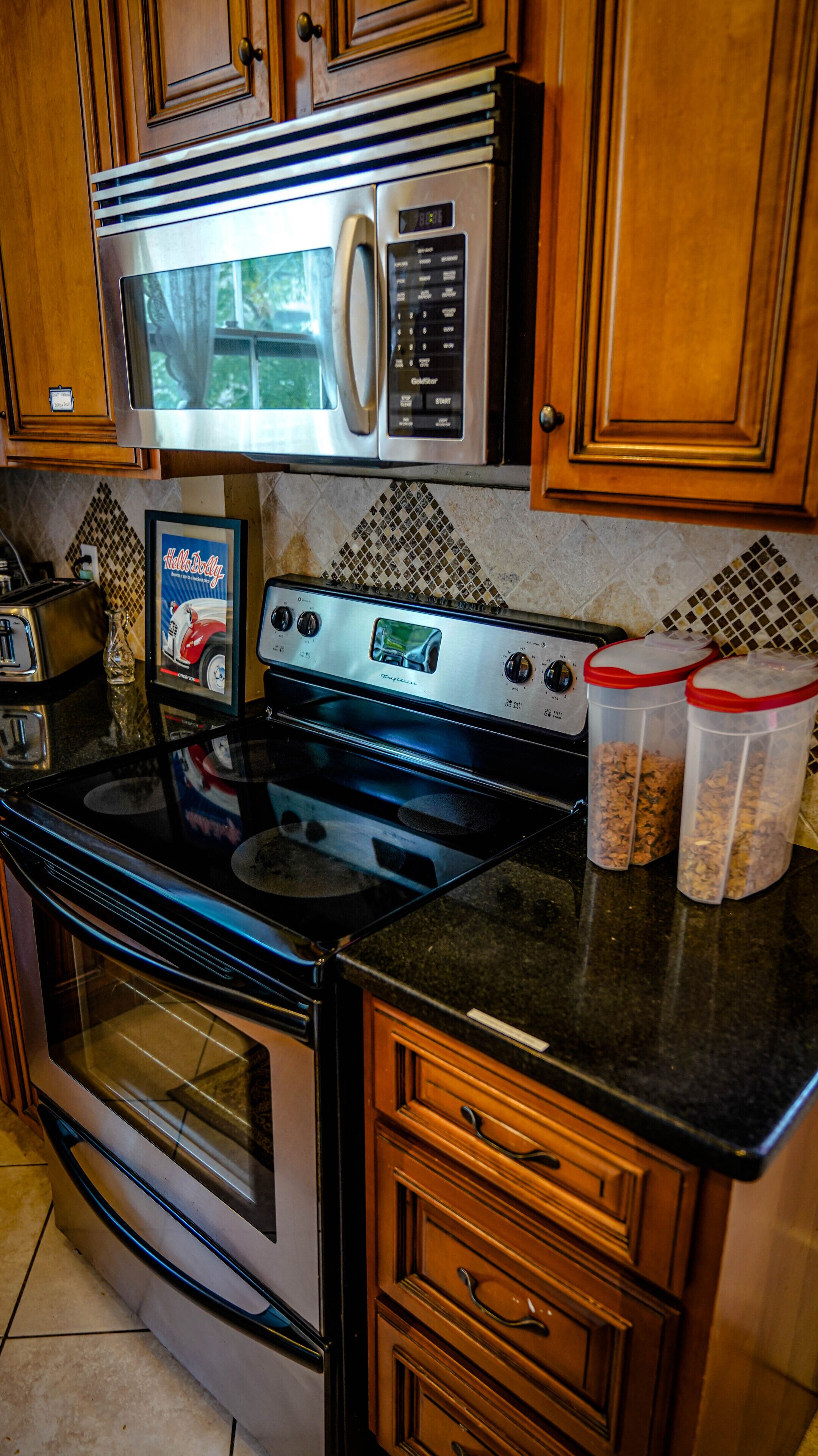 A kitchen with a stainless steel microwave, a digital stove, and wooden cabinets. There are two containers on the counter.