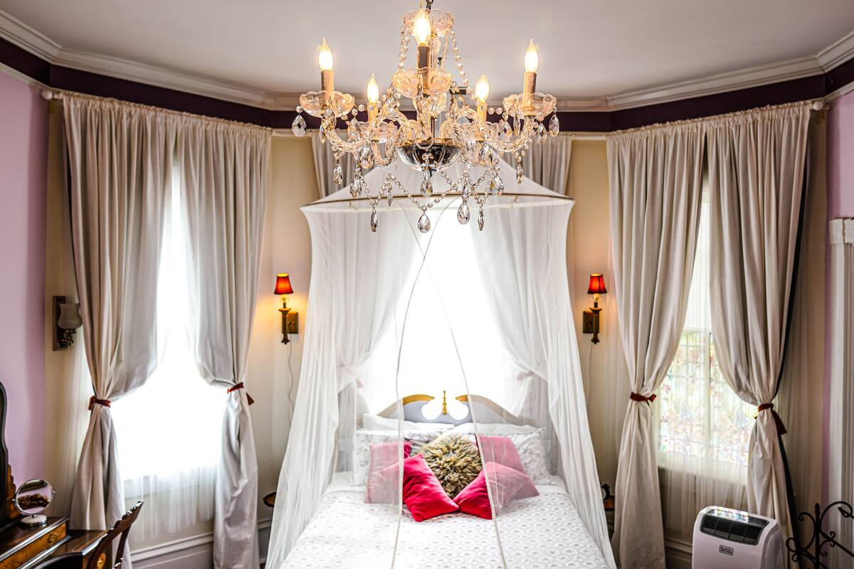 A bedroom with a canopy bed, a chandelier, and a large mirror.