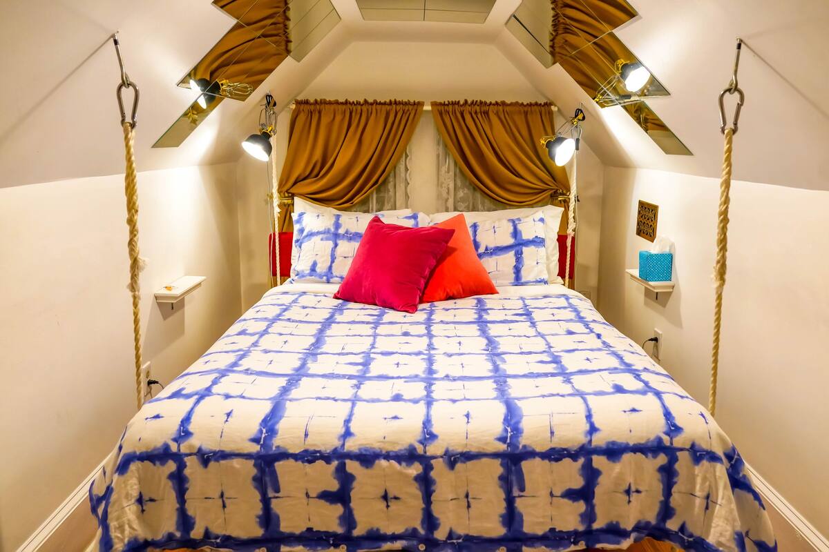 A bedroom with a bed, two bedside lamps, a nightstand, a mirror, and a window with curtains.