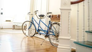 Una escalera con balaustres blancos y detalles azules, una bicicleta azul apoyada contra una pared, y un suelo de madera.