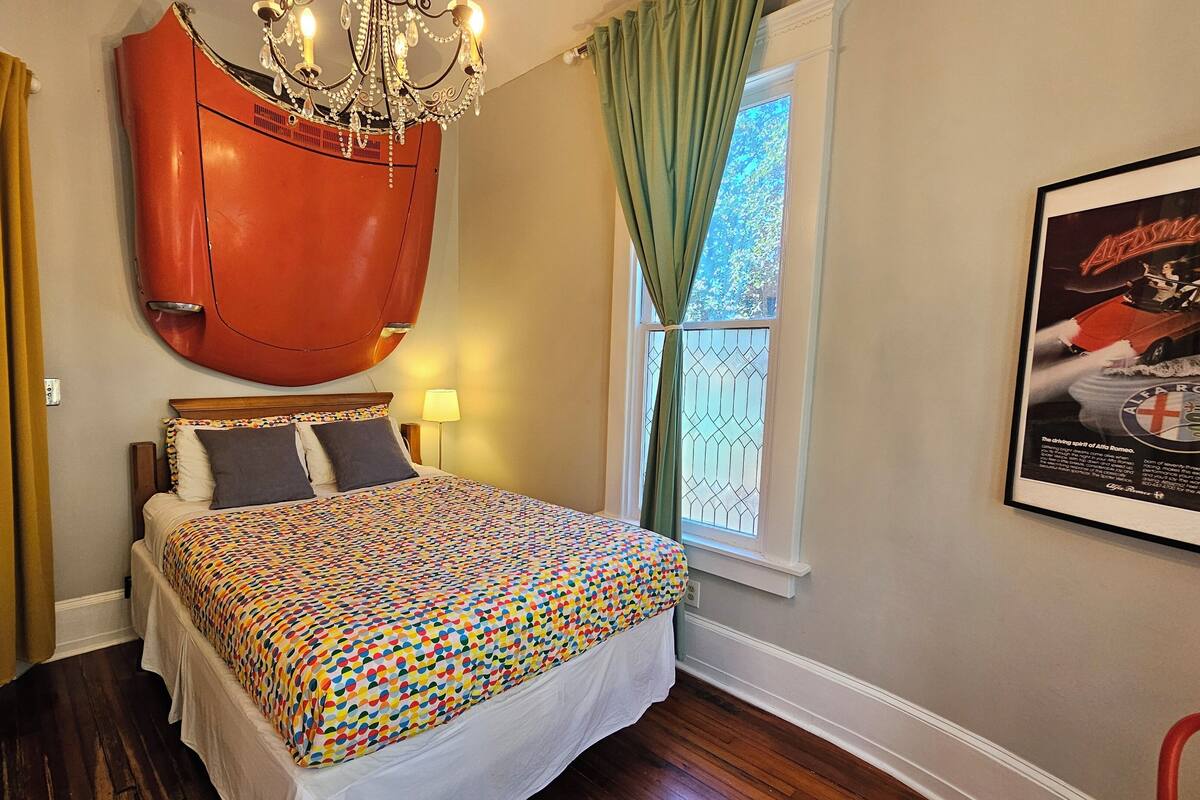 A bedroom with a bed, a chandelier, a window with curtains, and a poster on the wall.