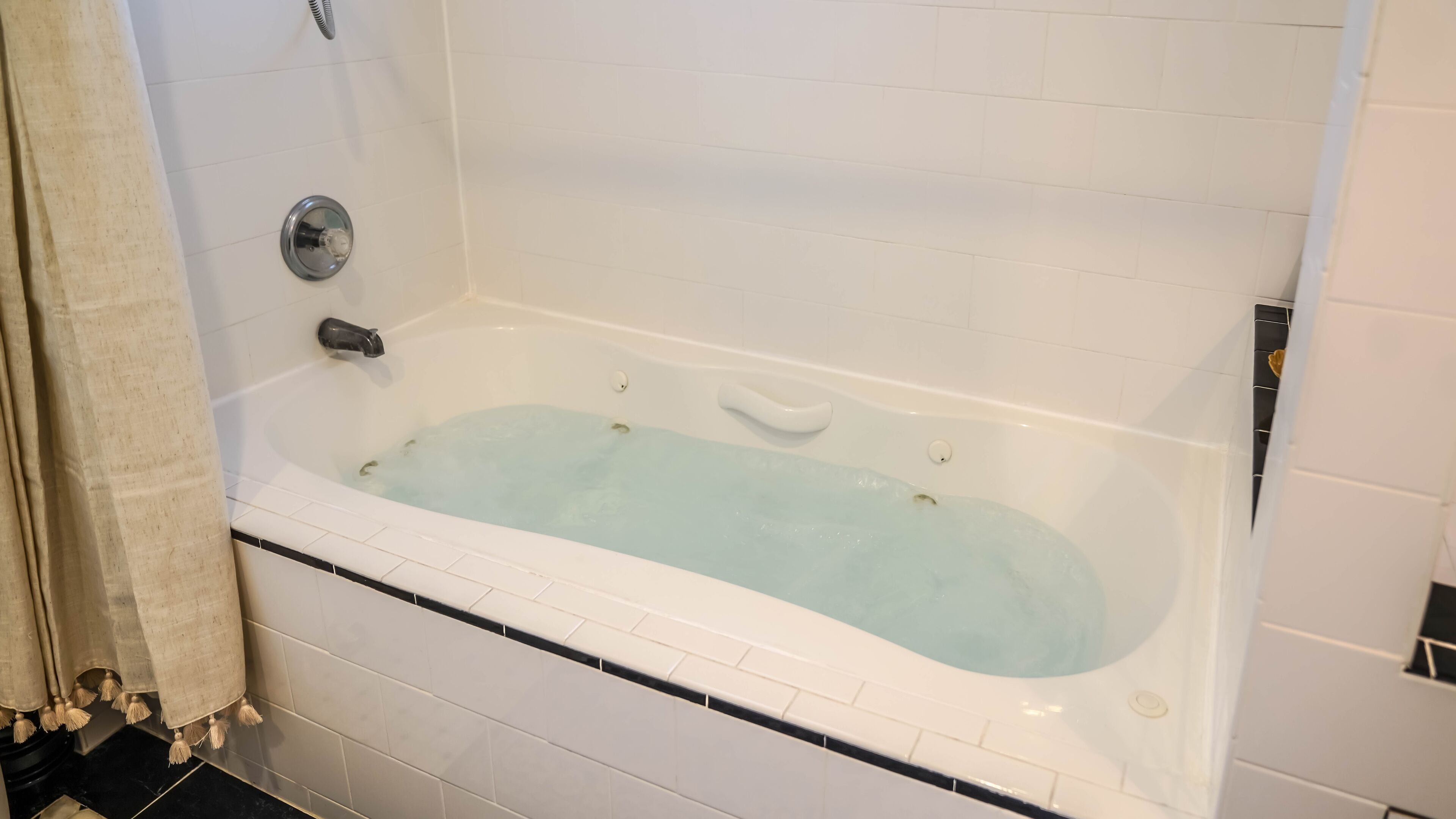 A bathtub with a white interior, a chrome faucet, and a control knob.