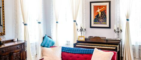 Una sala de estar con un sofá rojo, sillas azules, una araña de techo, un piano y un tapete estampado.