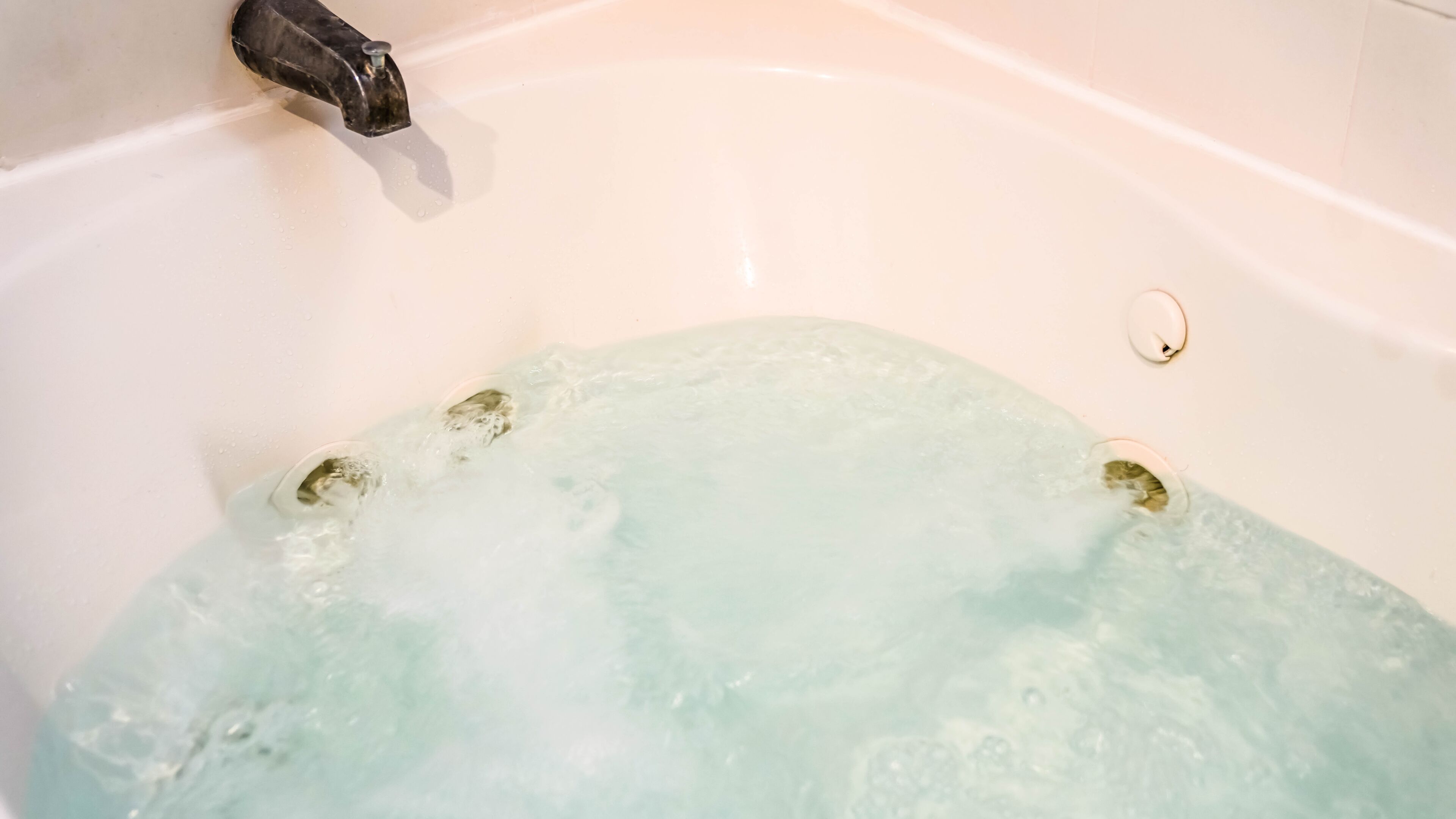 A bathtub filled with clear water, a faucet, and a drain plug.