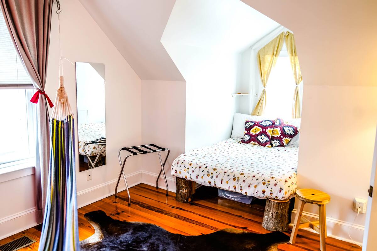 A bedroom with a bed, a hanging light fixture, a mirror, and a window with curtains.