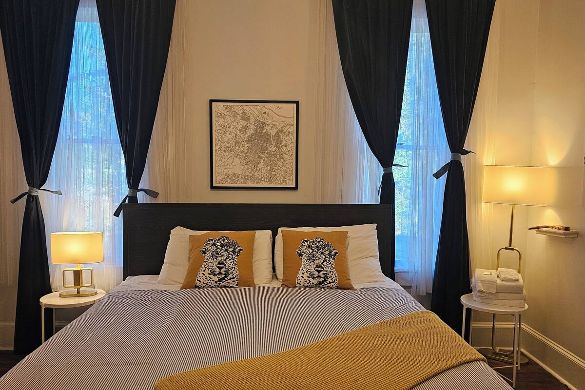 A hotel room with a large bed, two nightstands, a wall-mounted lamp, and a framed map.