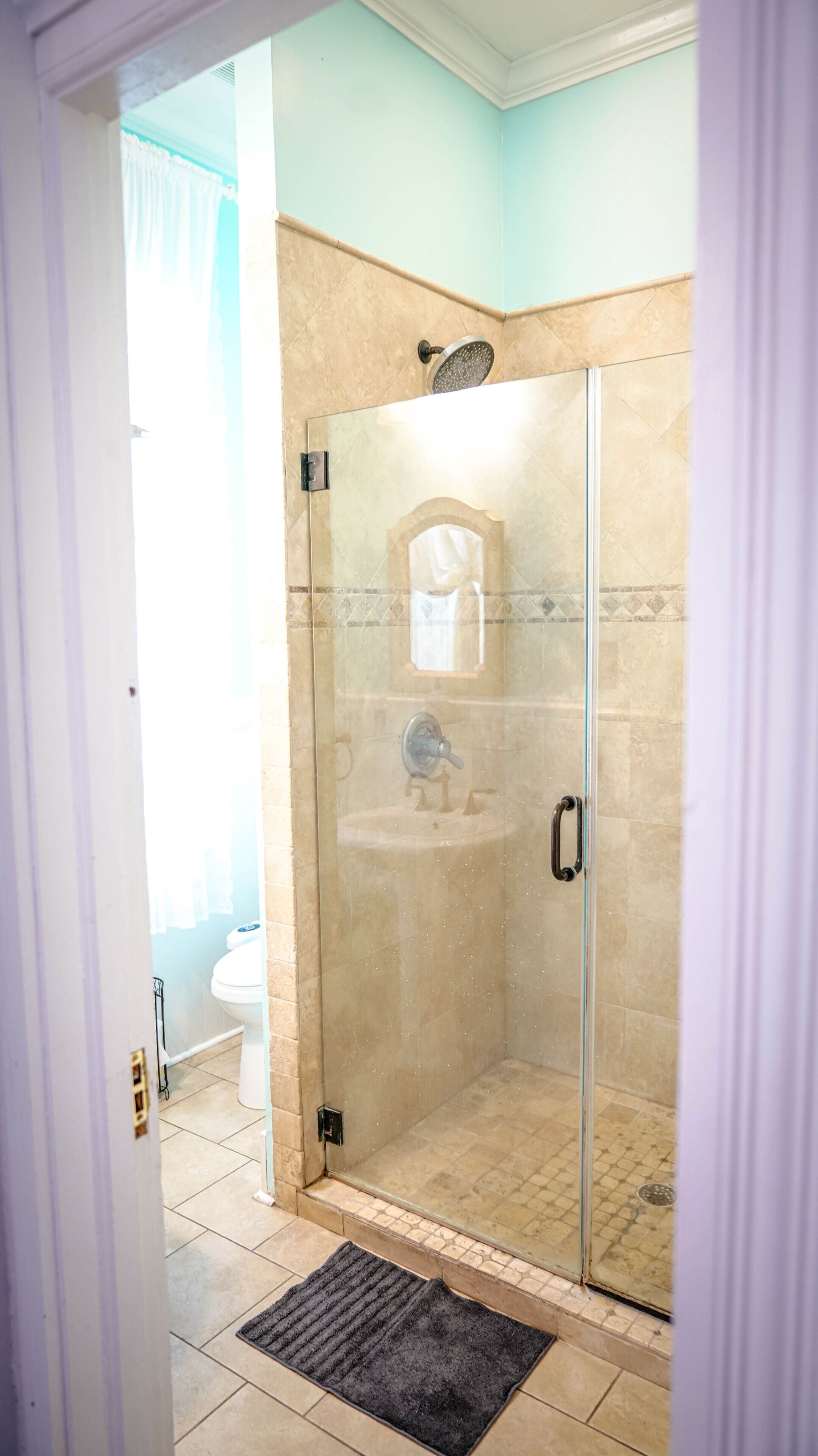A glass-enclosed shower with a beige tiled wall, a white sink, and a mirror above it.