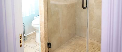 A glass-enclosed shower with a beige tiled wall, a white sink, and a mirror above it.