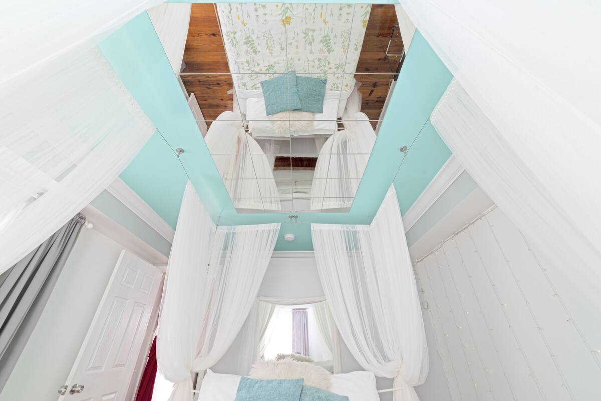 A bedroom with a canopy bed, a wooden ceiling, and a view of the outside through a window.