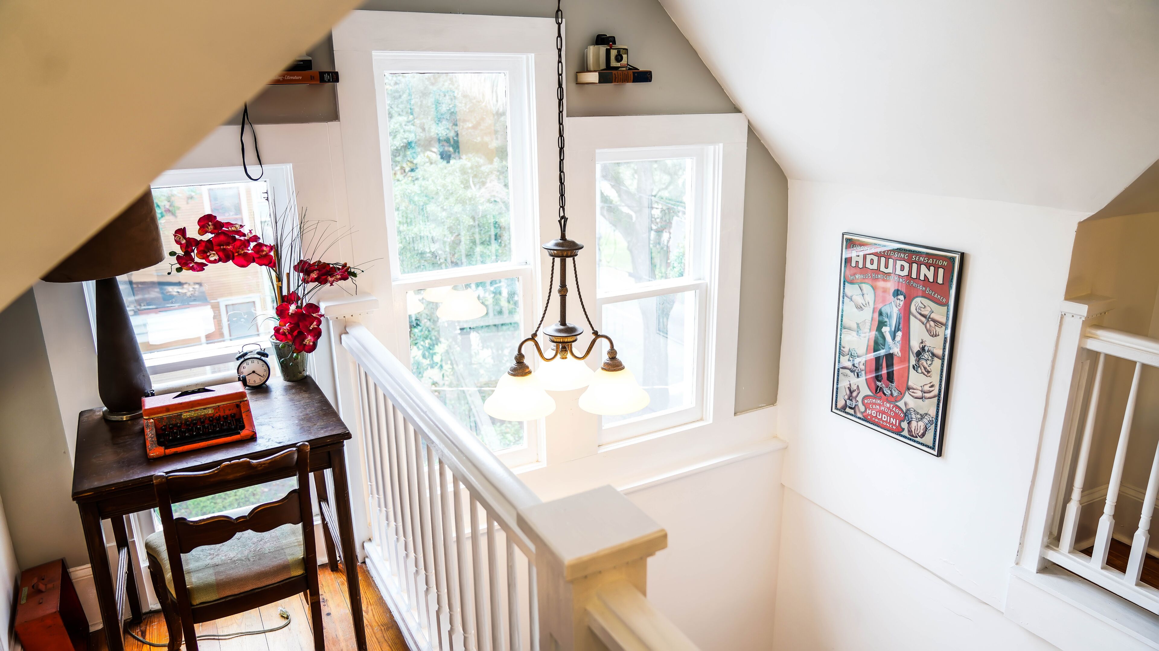 A staircase with a white railing, a wooden table with a clock and a keyboard, and a poster on the wall.