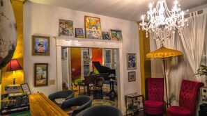 A living room with a grand piano, red chairs, a chandelier, and various framed artworks on the walls.