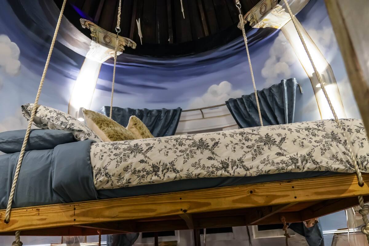 A bed suspended from the ceiling with a wooden frame, ropes, and a floral bedspread.