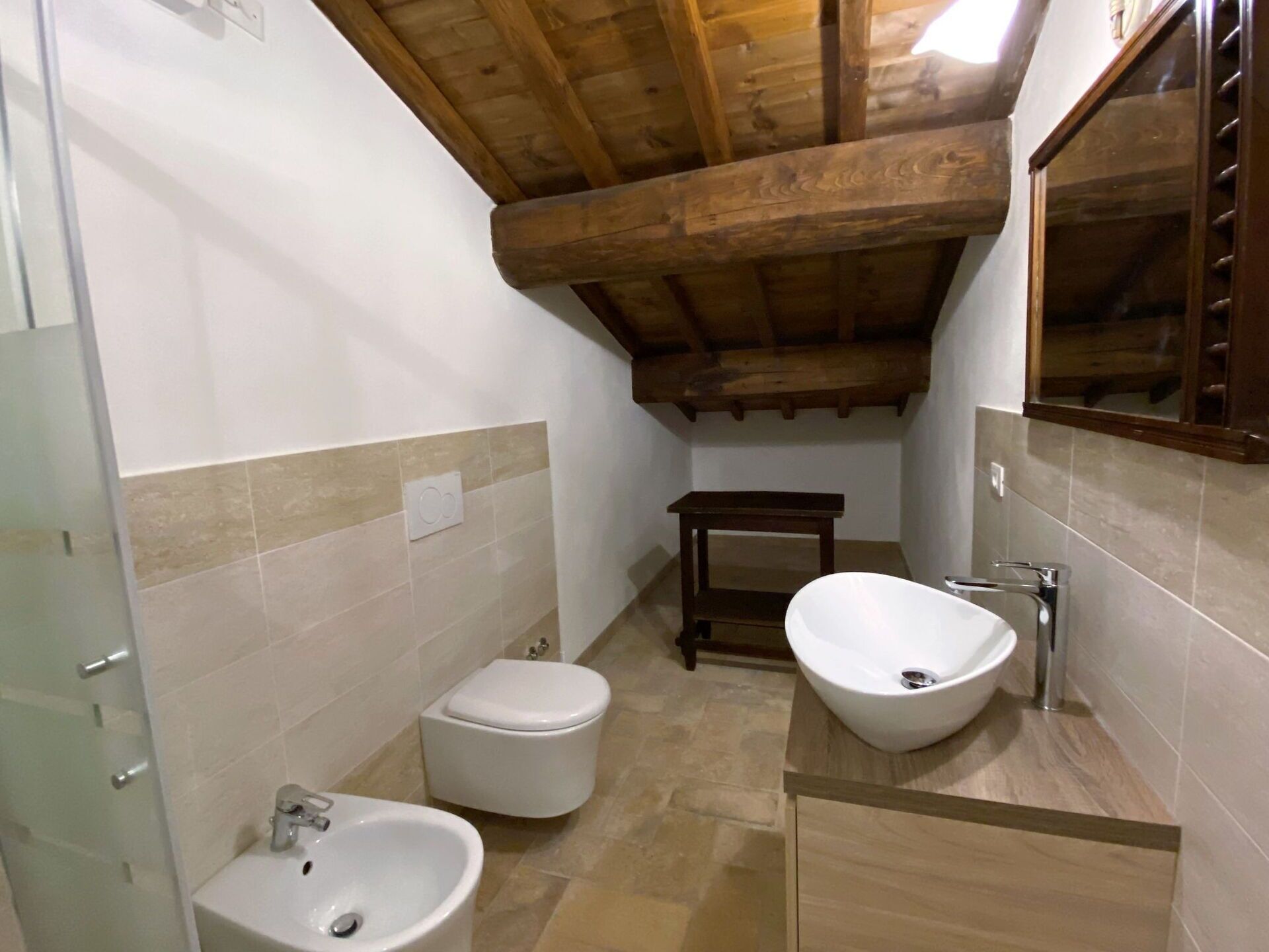 Une salle de bain avec un plafond en bois, des toilettes, un bidet et un lavabo avec un miroir au-dessus.