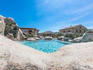 A clear blue pool surrounded by large rocks and traditional stone buildings.