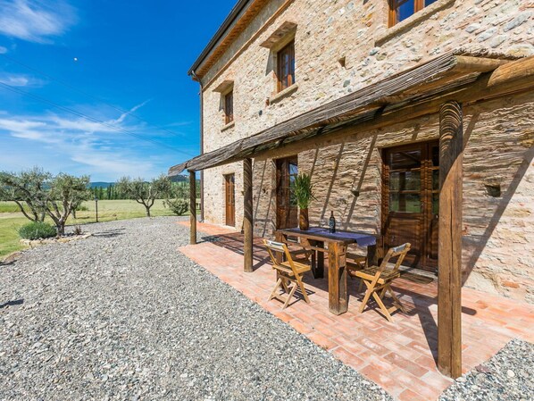 A stone building with a covered patio area featuring a table and chairs.