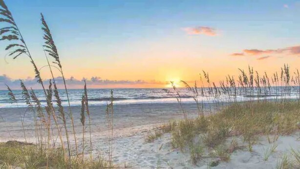 A beach with sand and grass, a sunset in the background, and waves. - ISLAND VIBE ~ Close to Beach, Downtown, Egan’s Creek with Fire Pit! KQQ~2Ba (Fernandina Beach)