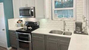 A modern kitchen with white cabinetry, a stainless steel microwave, a gas stove, and a double sink. - ISLAND VIBE ~ Close to Beach, Downtown, Egan’s Creek with Fire Pit! KQQ~2Ba (Fernandina Beach)