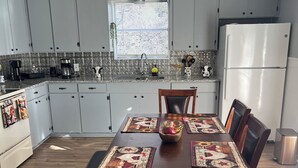 A kitchen with grey cabinets, a stainless steel refrigerator, a wooden dining table with placemats, and a window with blinds. - The CountryLake - First Floor for 7 Guest  (Belton)