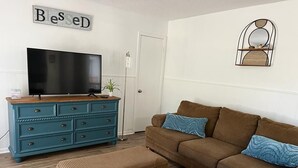 A living room with a brown sofa, matching ottoman, and a teal dresser. A flat-screen TV is on the dresser, and a decorative mirror hangs on the wall. - The CountryLake - First Floor for 7 Guest  (Belton)