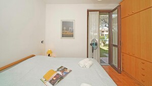 Ein Schlafzimmer mit Bett, einem fenster mit Vorhängen, einem Holzschrank und einem kleinen Tisch mit Lampe.