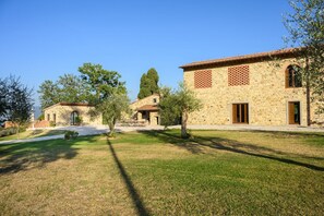 Un bâtiment en pierre avec un toit en tuiles, un petit jardin et un ciel dégagé.
