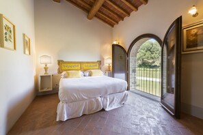 Ein Schlafzimmer mit Bett, Nachttisch, Lampe, Fenster mit Blick ins Grüne und einer Tür.
