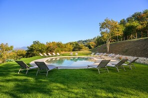 A circular pool with lounge chairs arranged around it, surrounded by a grassy area and trees. - Villa San Cresci by MMega (Vicchio)