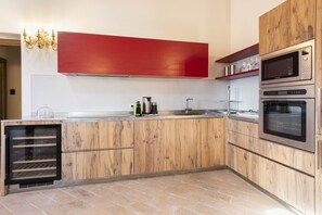 A modern kitchen with wooden cabinetry, stainless steel appliances, and a red accent wall. - Villa San Cresci by MMega (Vicchio)