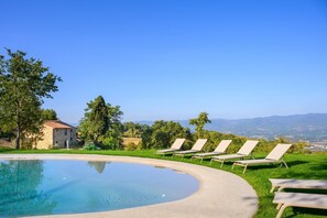 A swimming pool with lounge chairs, a stone building, and a view of the landscape.