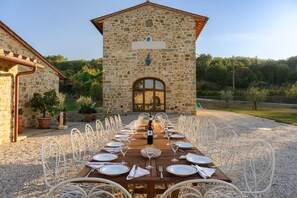 Un bâtiment en pierre avec une table en bois dressée pour le repas, entourée de chaises blanches.