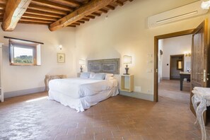A bedroom with a large bed, wooden beams, a window, and a door leading to another room.