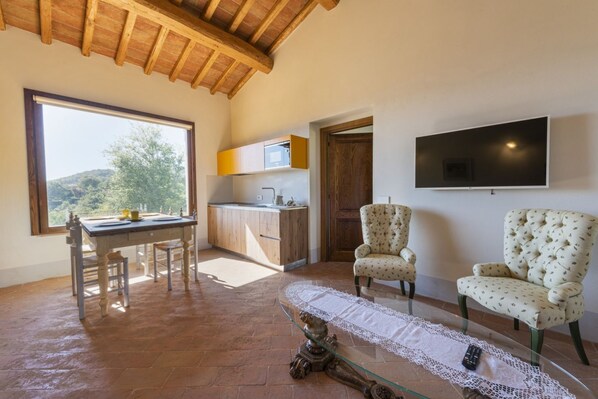 A spacious room with a dining table, two chairs, a TV mounted on the wall, and a view of the outdoors.