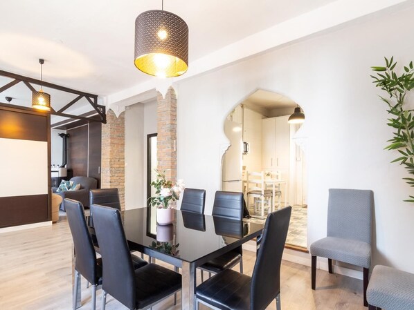 A modern dining area with a glass table, black chairs, and a hanging light fixture.