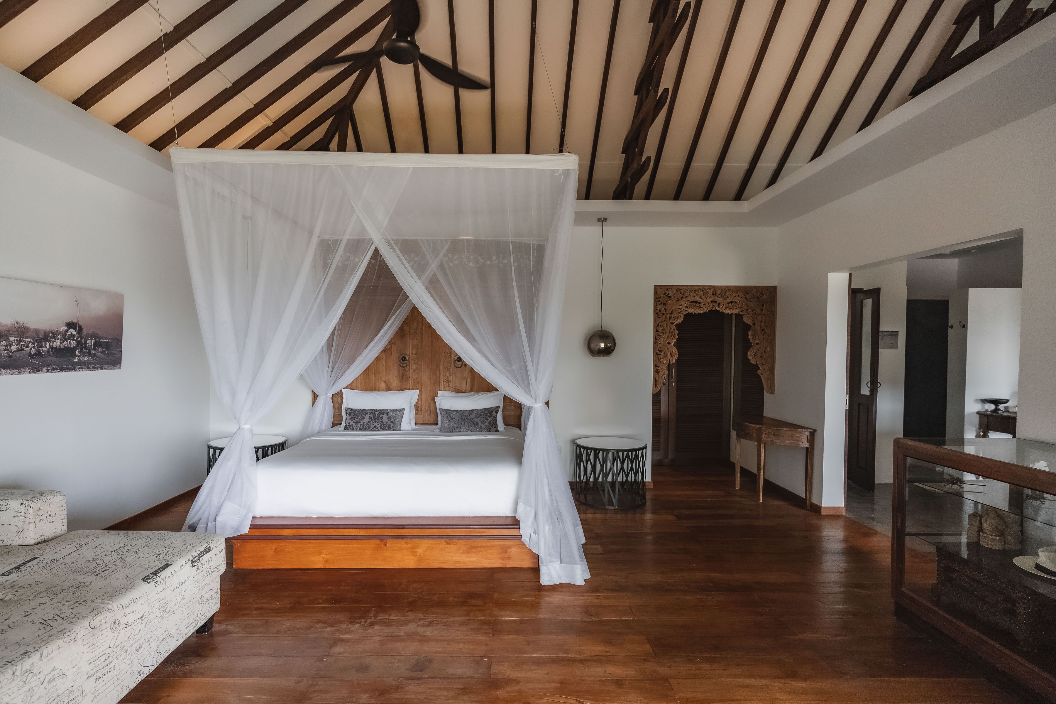 A bedroom with a canopy bed, wooden flooring, a ceiling fan, and a small round table.