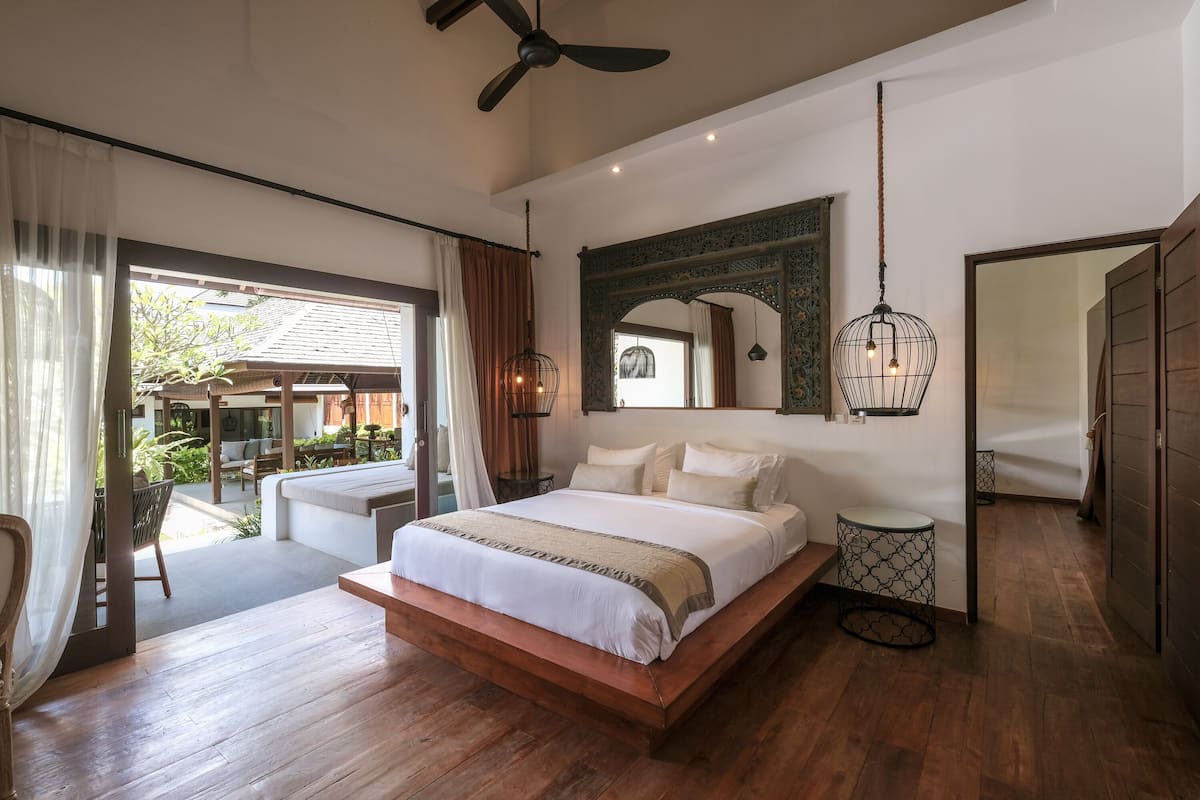 A spacious bedroom with a large bed, wooden flooring, a ceiling fan, and a view of the outdoor area.