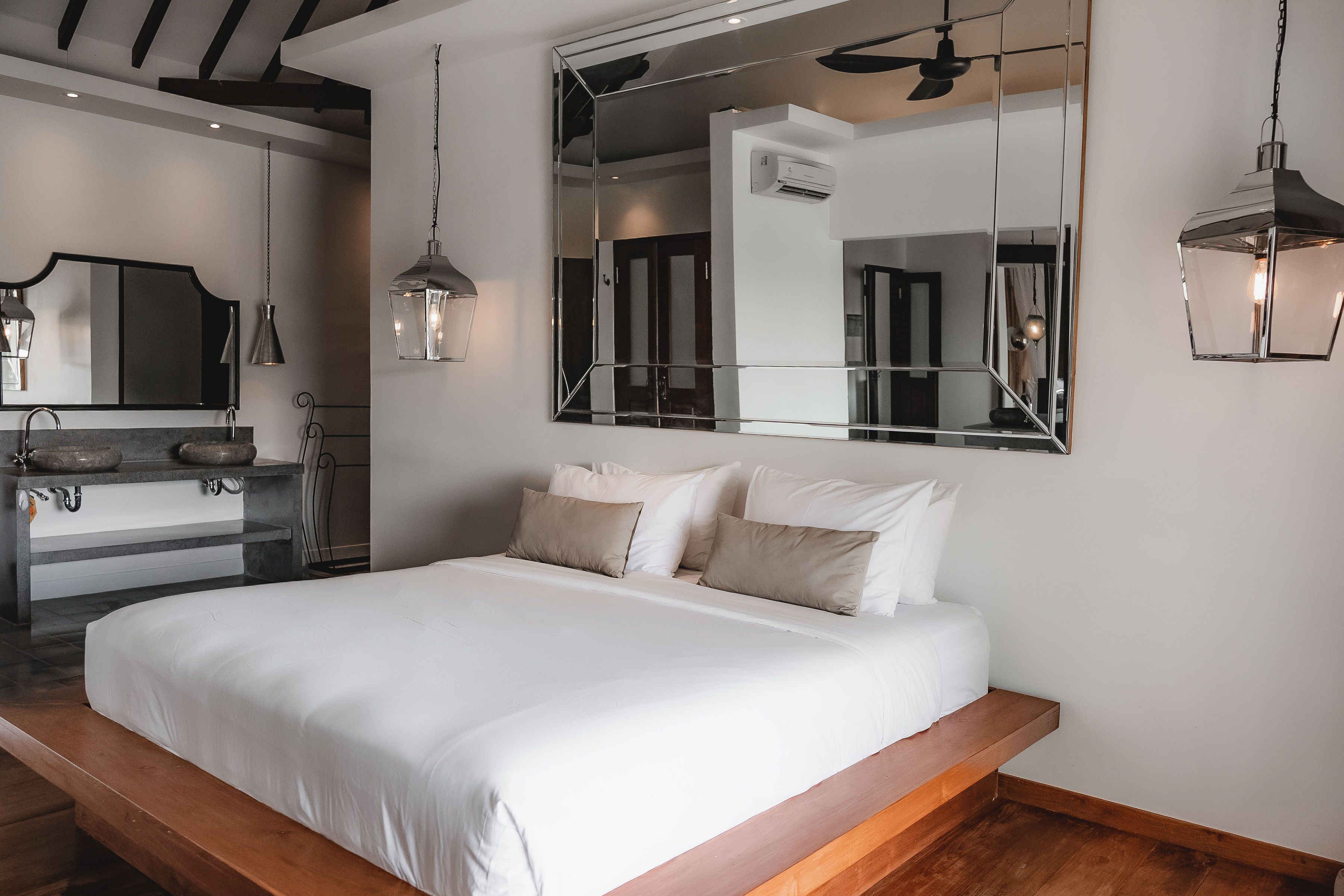 A bedroom with a large bed, a wooden platform, a mirror, and pendant lights.