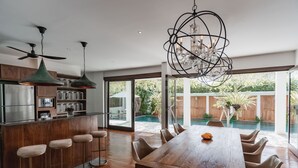 A modern kitchen with a wooden island, bar stools, and a dining area with a large table and chairs. - Aram Residence (Canggu)