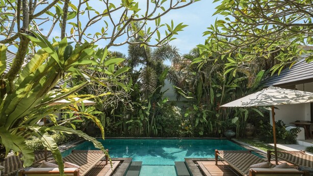 A pool area with wooden deck, lounge chairs, and a view of the pool. - Aram Residence (Canggu)