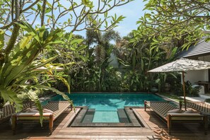 A pool area with wooden deck, lounge chairs, and a view of the pool. - Aram Residence (Canggu)