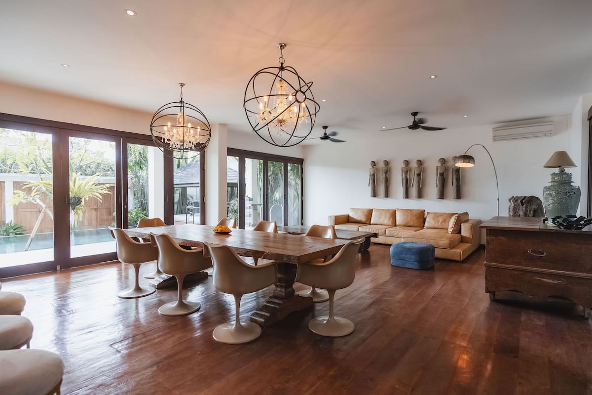 A spacious living area with a wooden dining table, modern chairs, a sofa, and a ceiling fan.