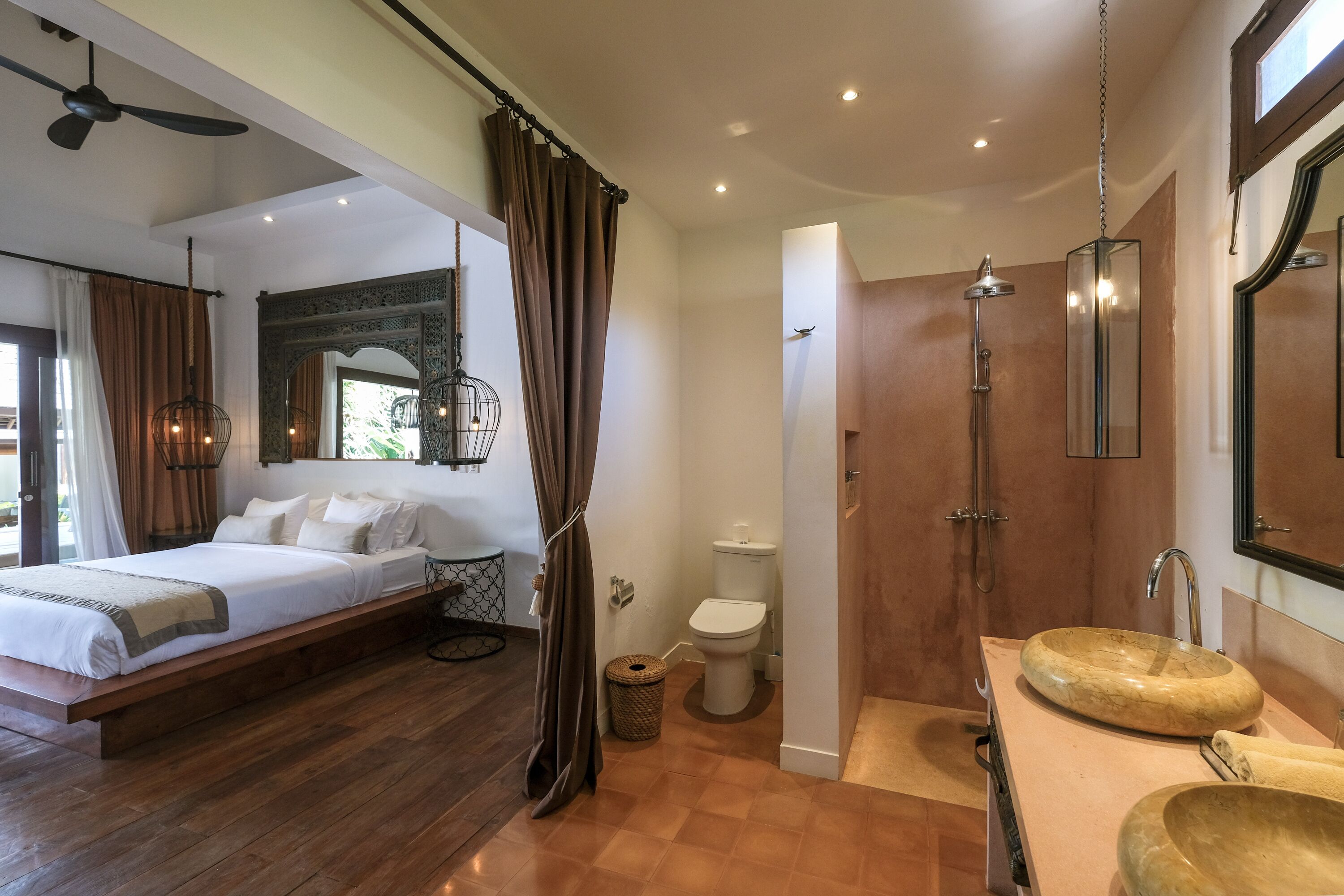 Quarto moderno com uma cama grande, banheiro com chuveiro em box de vidro e toucador de madeira com cuba.