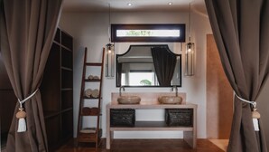 A bathroom with a wooden vanity, a mirror, and a shelf with towels. - Aram Residence (Canggu)
