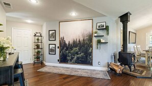 A living room with a large forest mural, a black wood-burning stove, and a dining area with a table and chairs. - Yosemite, Hot Tub, Pets - Memories! (Oakhurst)