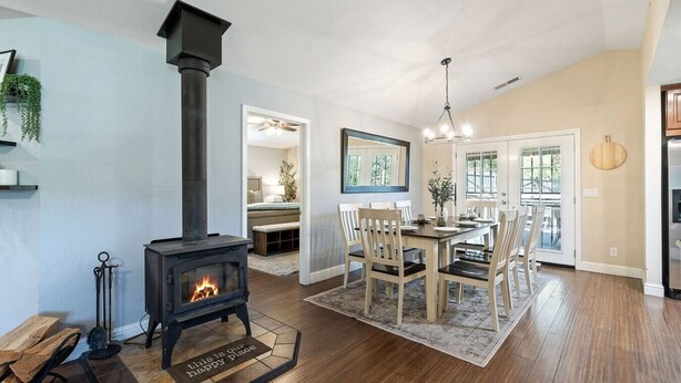 A cozy living room with a wood-burning stove, a dining area with a wooden table and chairs, and a kitchen visible through an open door. - Yosemite, Hot Tub, Pets - Memories! (Oakhurst)