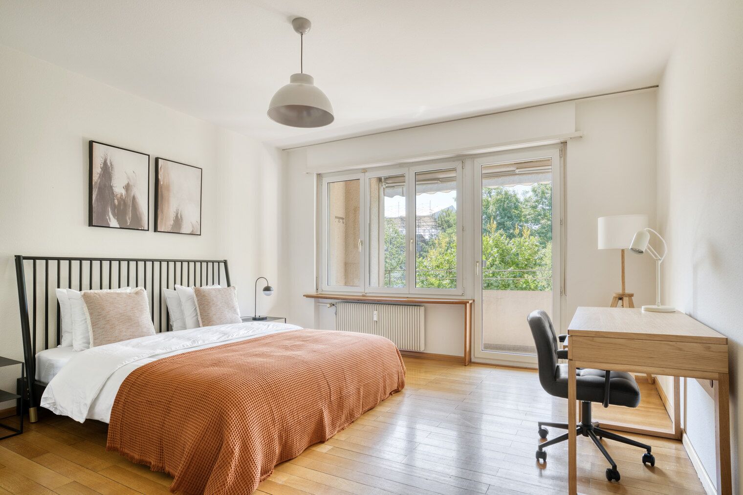 A bedroom with a bed, a desk, a chair, a window, and artwork on the wall.