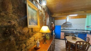 Une cuisine rustique aux murs de pierre, avec des meubles en bois et un coin repas comprenant des chaises et une table.