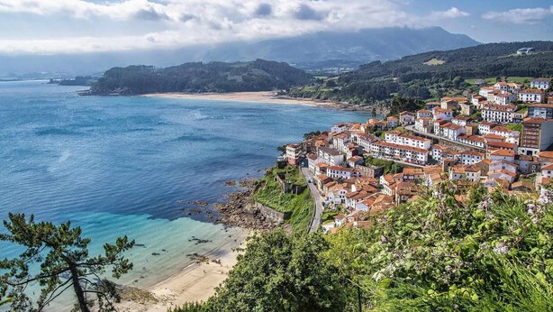 Une ville côtière avec des maisons à étages, une plage et une montagne en arrière-plan.