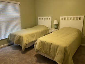 A room with two single beds, a nightstand with a lamp, and a window with blinds. - Sea Colony 2 BR, Screened Porch, Steps to Pool, Pickleball, Tennis (Bethany Beach)