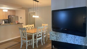 Una cocina moderna con armarios de madera, un refrigerador empotrado, una mesa de comedor con sillas y un televisor de pantalla plana montado en una pared de acento de mármol.