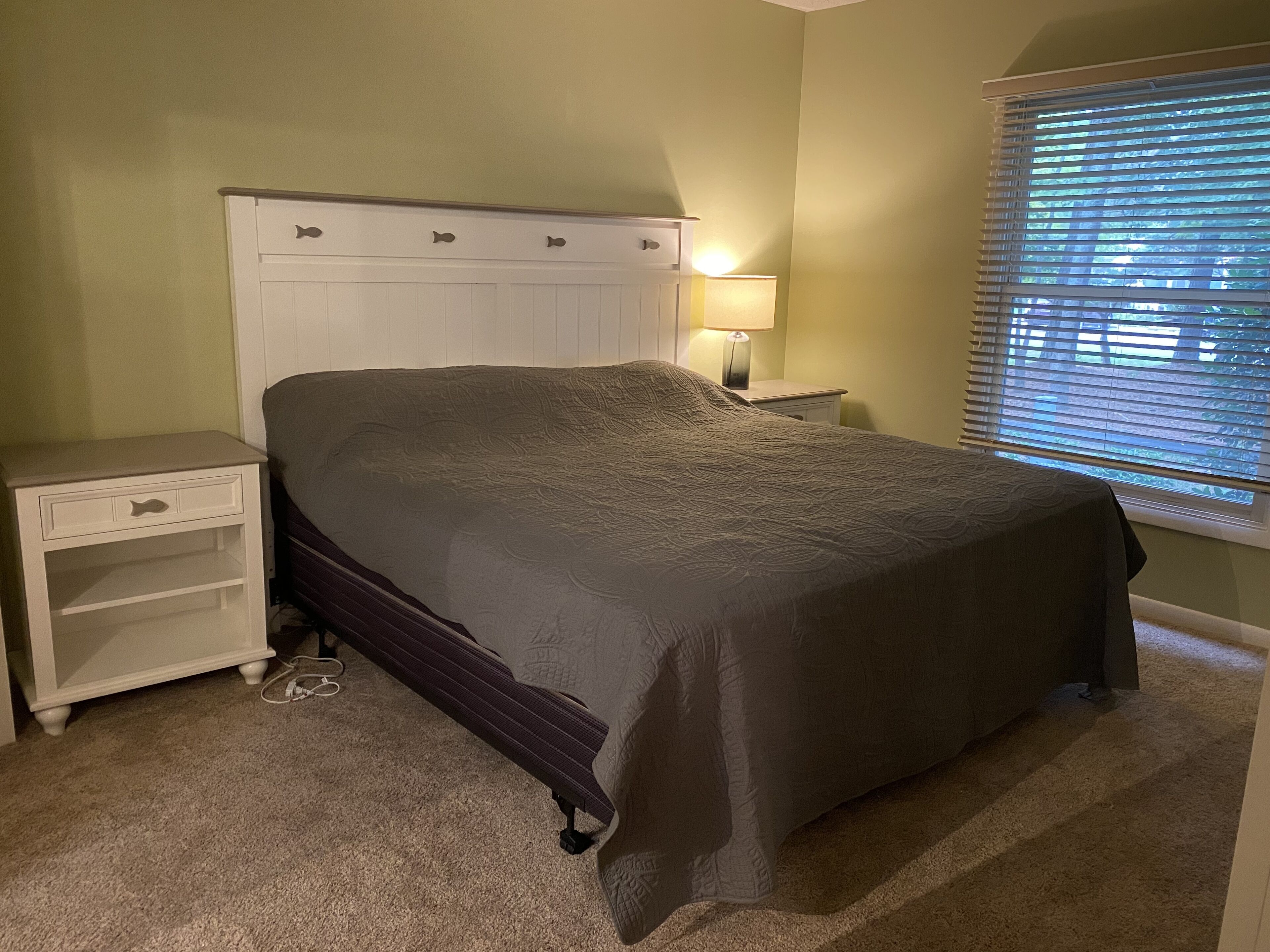 A bedroom with a bed, nightstand, lamp, and window with blinds.